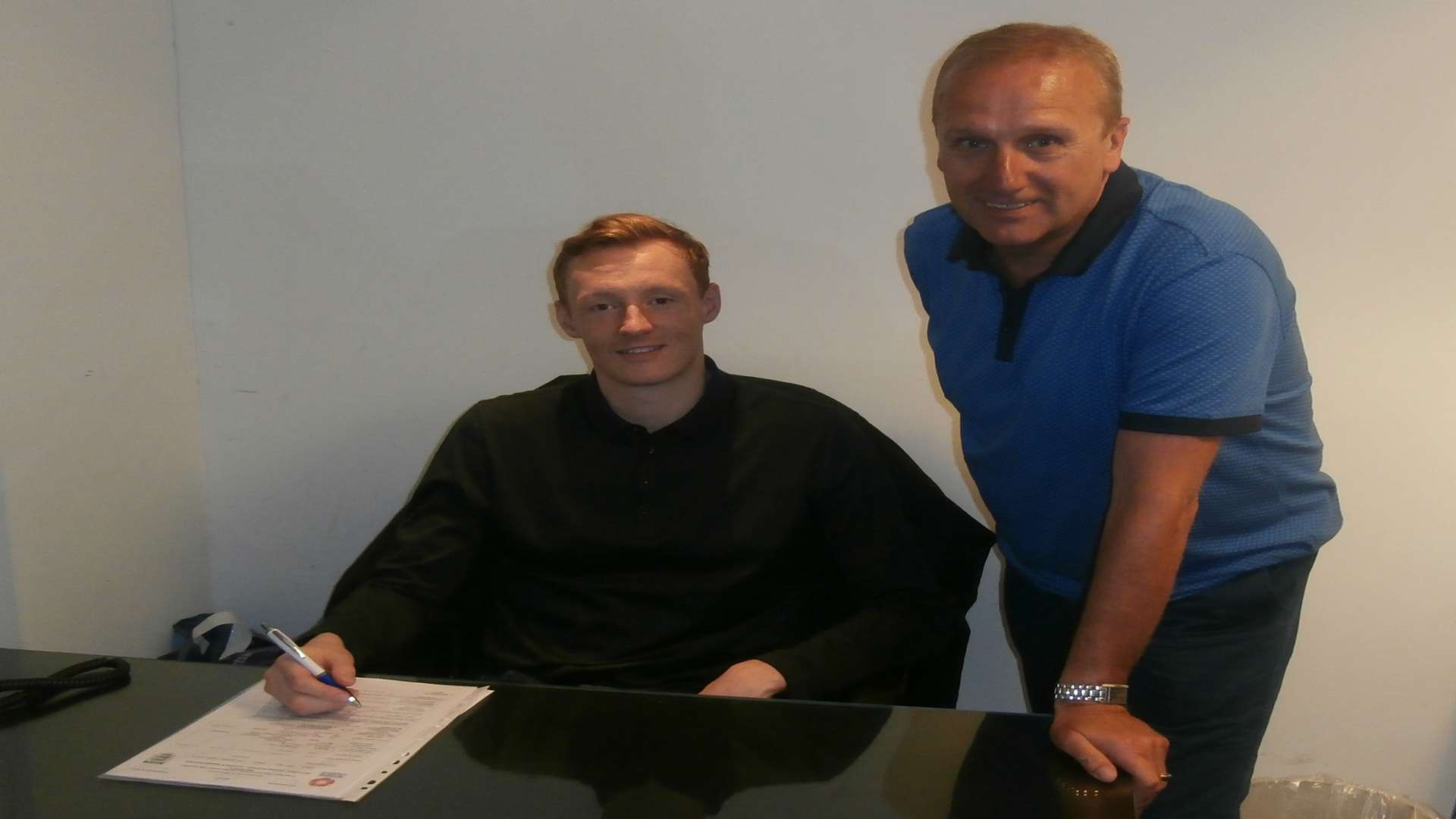 Dartford's new defender Callum McNaughton signs his contract with manager Tony Burman
