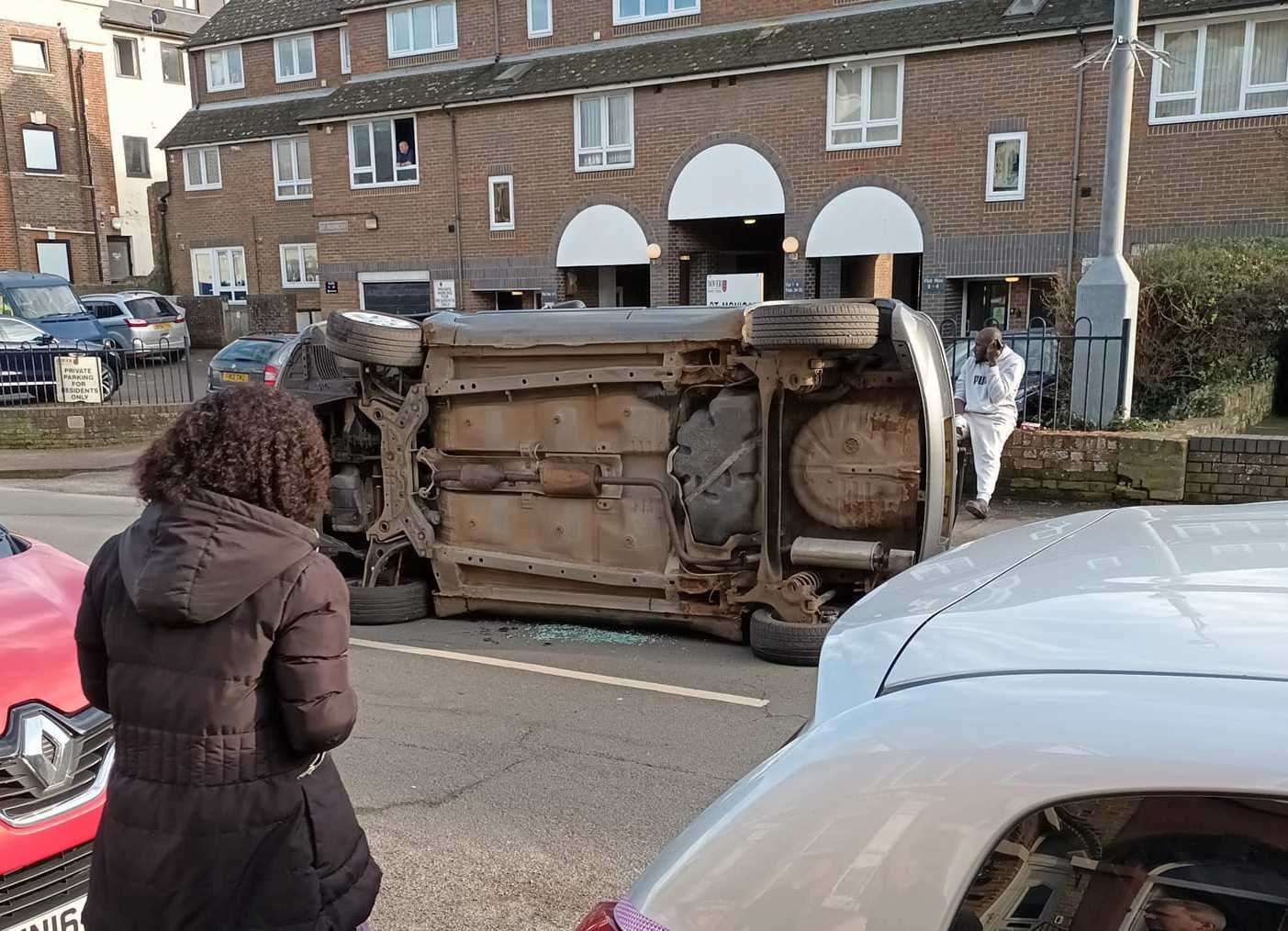 The car on its side just after the crash at Folkestone Road, Dover. bystander looks on