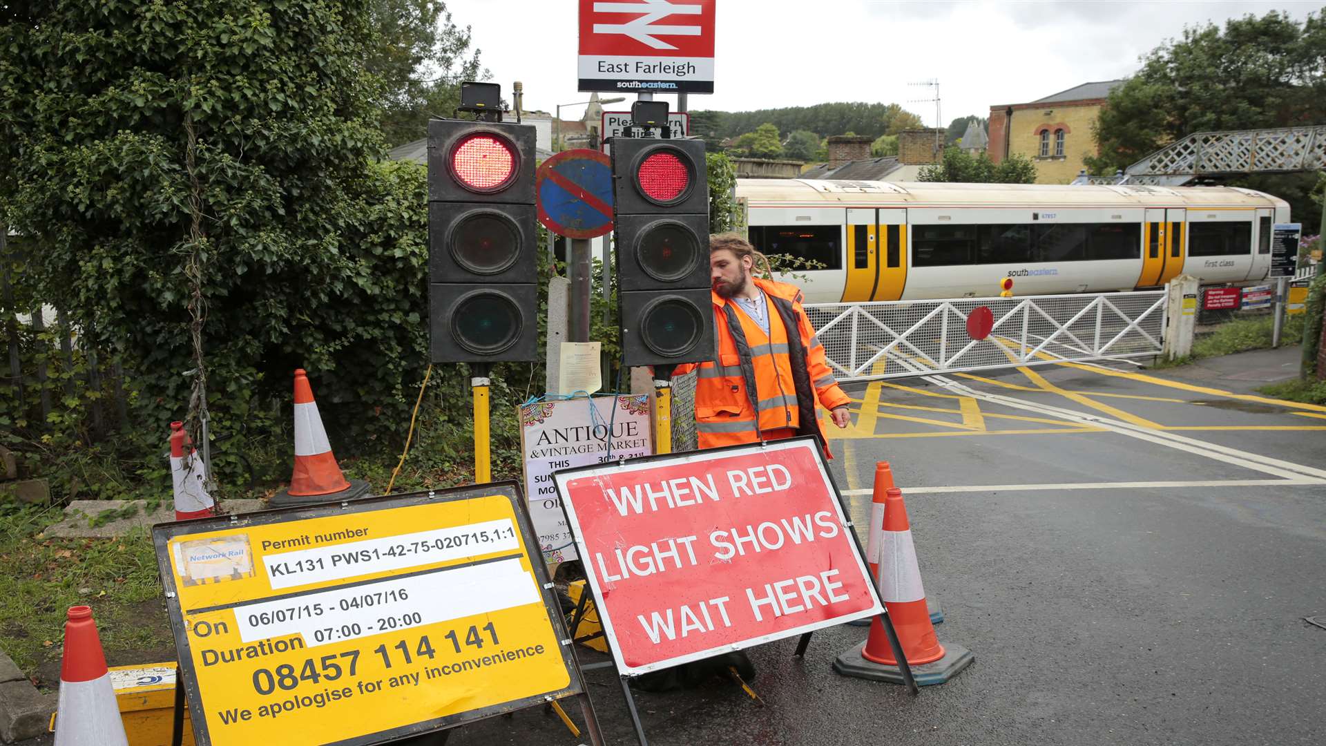 A worker from Centurion Transport LTD activating the traffic lights ahead of a train passing East Fairleigh level crossing, opening and closing the gates for traffic.