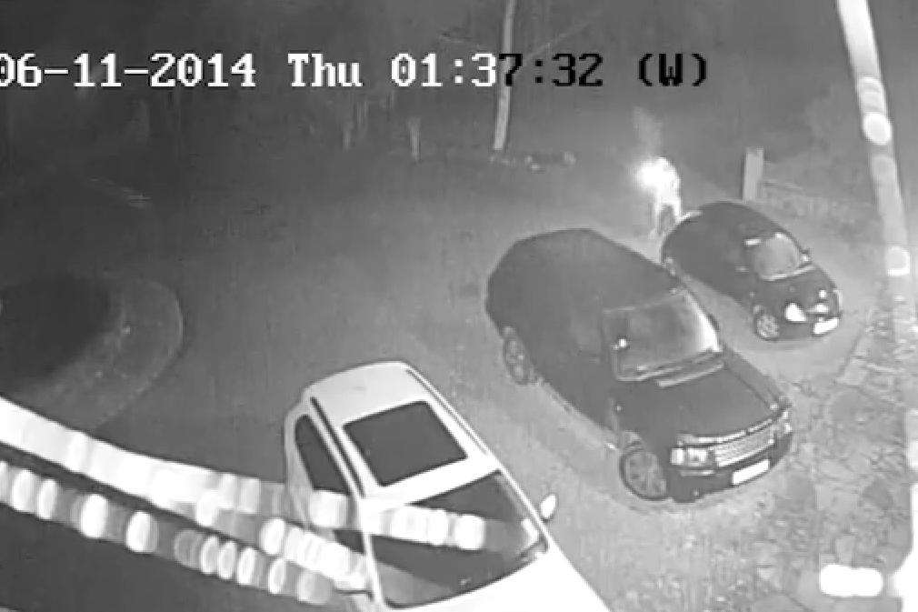 The other suspect lights an item before throwing it into the car.