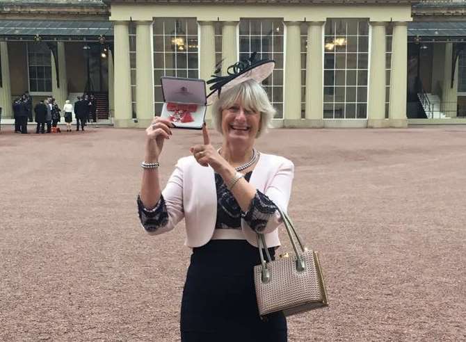 Proud Sue Clark MBE shows of her award outside Buckingham Palace