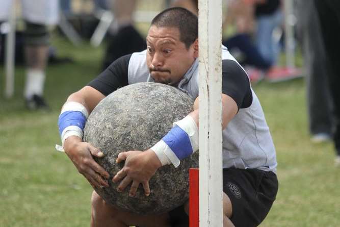 Bobby Glover, looks as if he is playing a bizarre game of volleyball with a very heavy stone ball when he is actually just lifting it over a tall bar at a strongman competition at Gravesend Town Regatta and Fusion Festival.