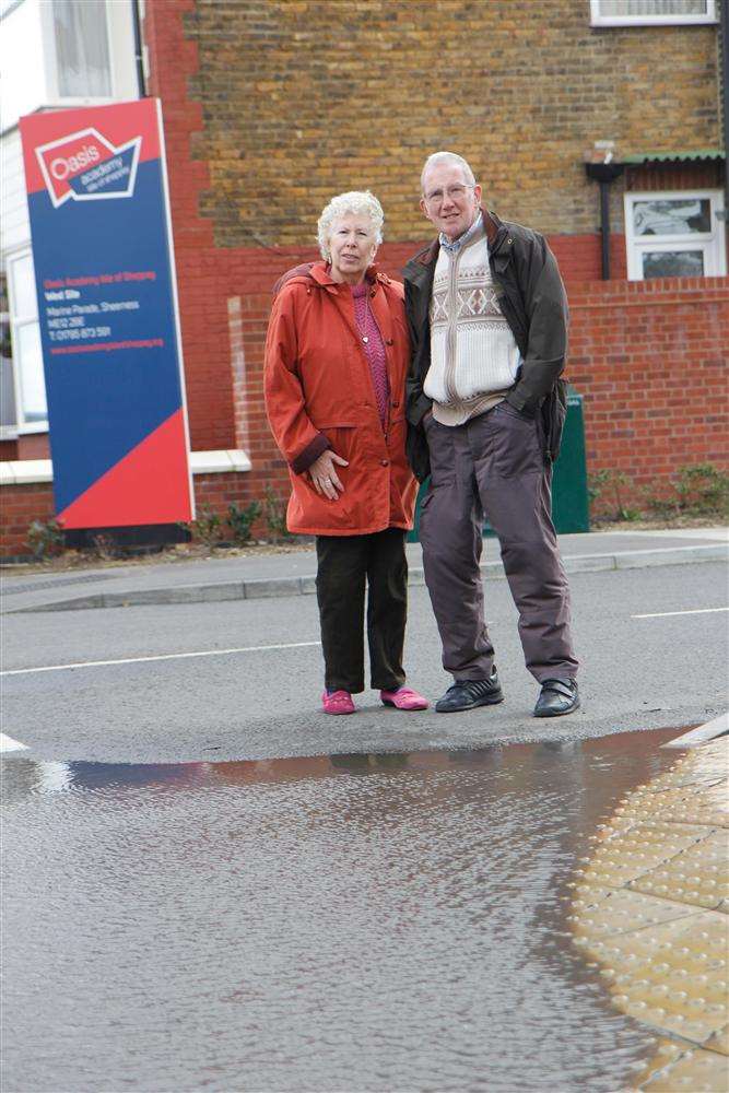 Joyce and Douglas Cole at the entrance to the Oasis Academy Isle of Sheppey in Marine Parade, Sheerness, with the massive puddle that forms at the dropped kerb