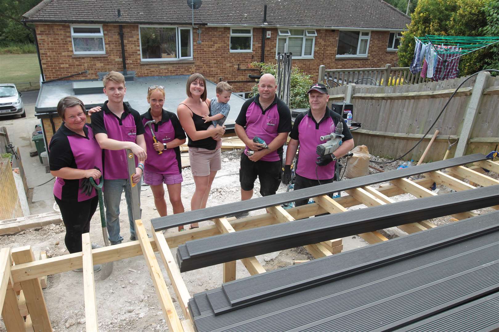 From left, Kirsty Selves with her son Louie, two, centre with Ilona Verba, Brencer Babrian, Sophie Opavszky, Imre Babrian and Paul Cartwright, two teams from Allington and Newington "Hire a Hubby" franchise helping to build decking for Trinity the disabled daughter of Kirsty, who was at school while the teams did the garden in the Chatham area. Picture by: John Westhrop. (2891711)
