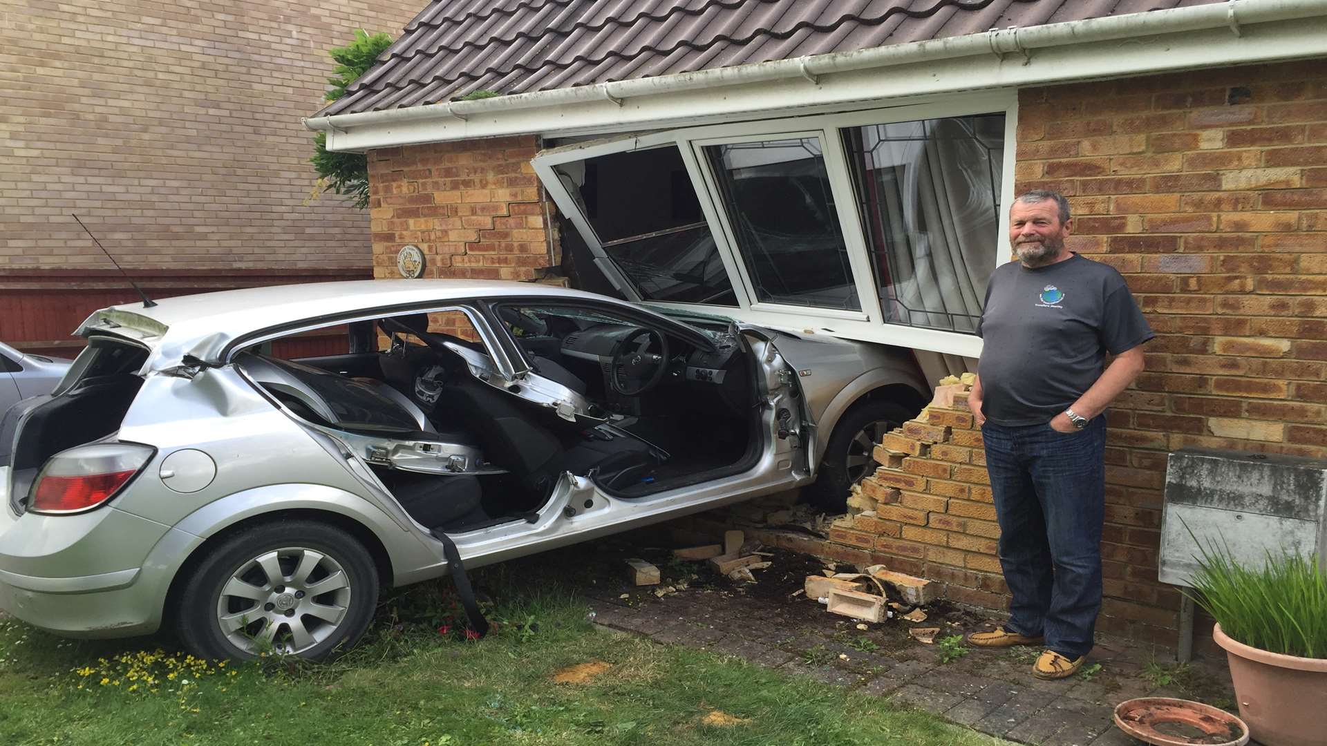 Pensioner Alan Kemp beside the car that ploughed through his living room window last night