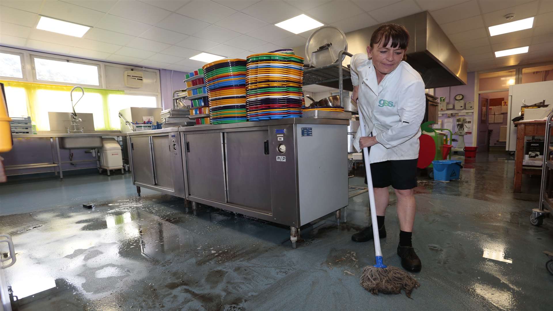 Clare Bush cleans the school's kitchen which will have to be fully sanitized after three inches of flood water left sediment covering the floor