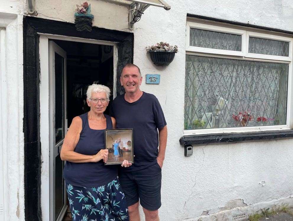 Jan and Jamie outside number 13 Acorn Street with a picture of their mum and dad