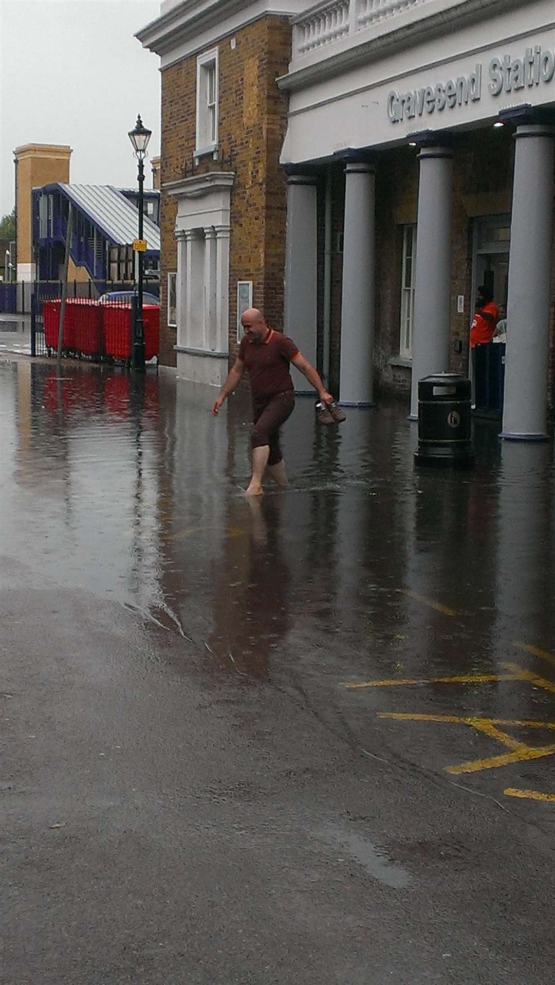 A passenger wades barefoot through the flood at Gravesend station on Sunday evening.