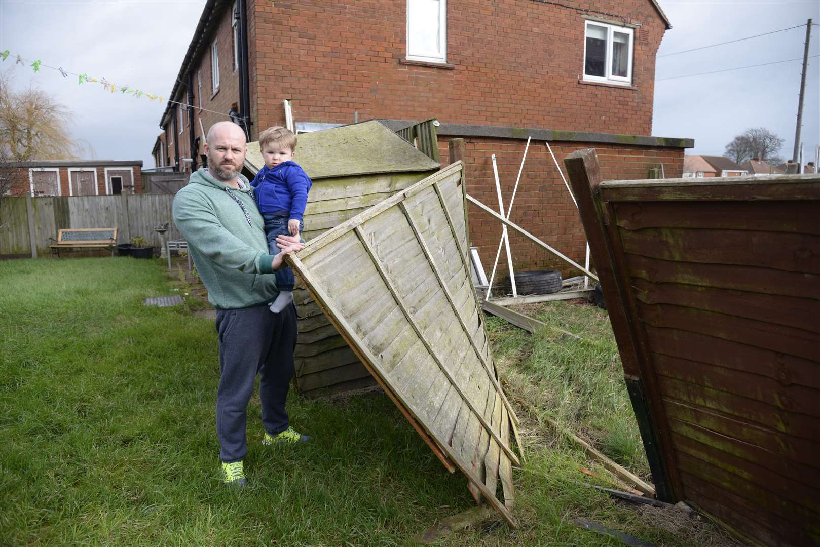 Paul Arnold and son 19-month son Harry with the damaged fence that seperates his garden from a neighbour who has five dogs