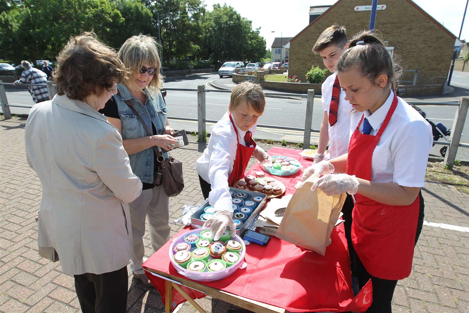 (ltor) Nell and Irina Warwick buy cakes from Jack Edgett and Jordan Collins, both 13, and Belle Peck,12, from Oasis Academy's "We Bake You Buy" team.