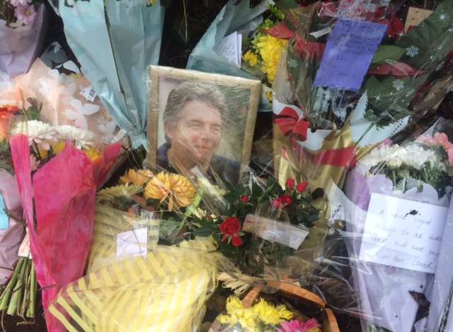 A photo sits between bouquets of floral tributes left at the scene of the fatal crash in Ash Road, New Ash Green