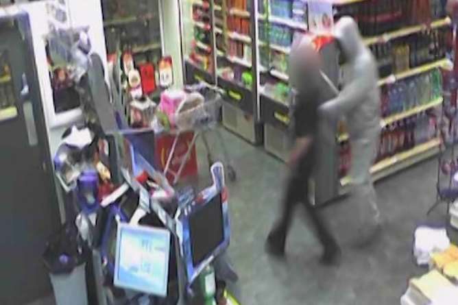 One of the robbers grabs a newsagents staff member