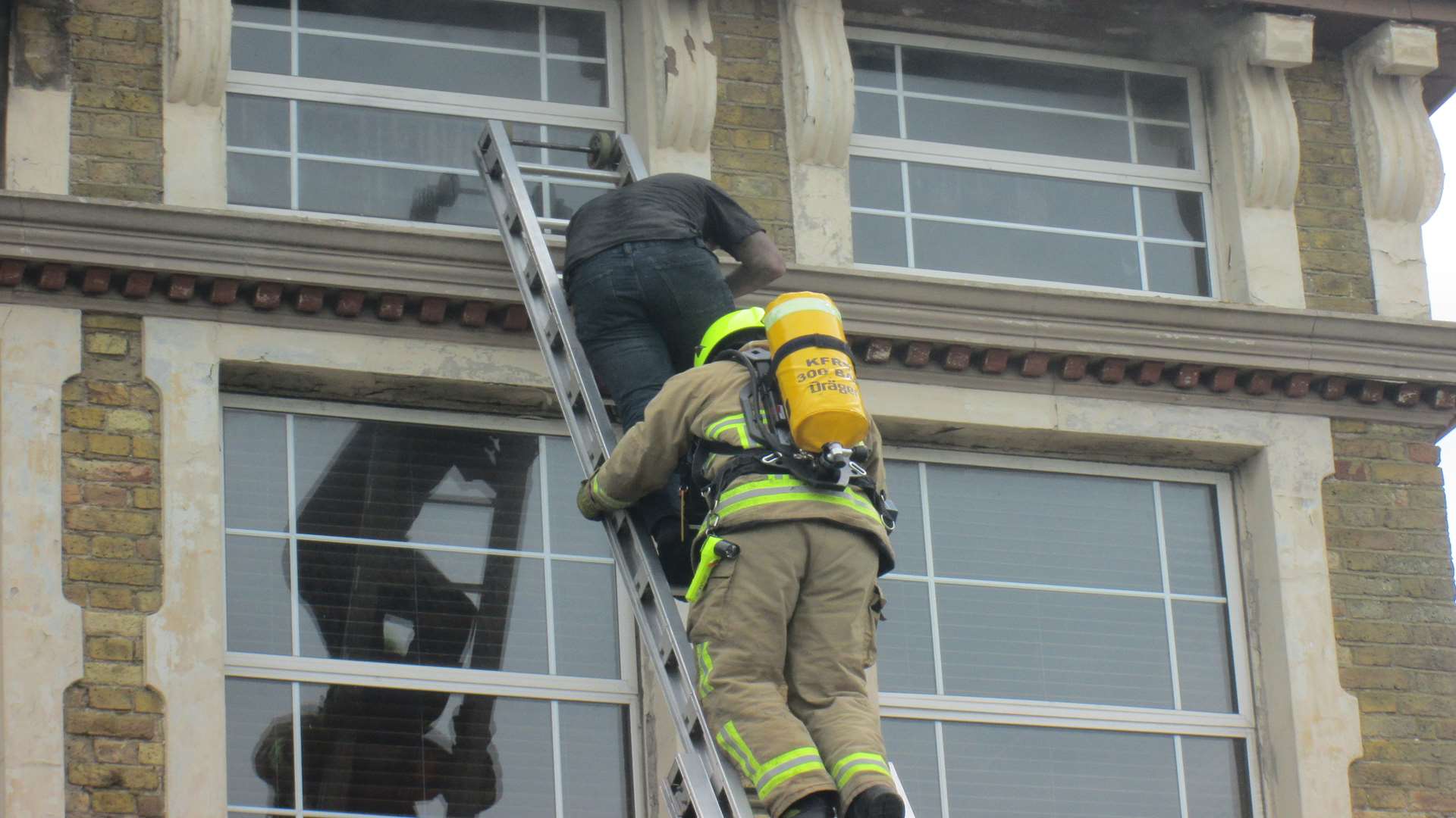 A man is brought down by ladder from the top floor of the blazing building