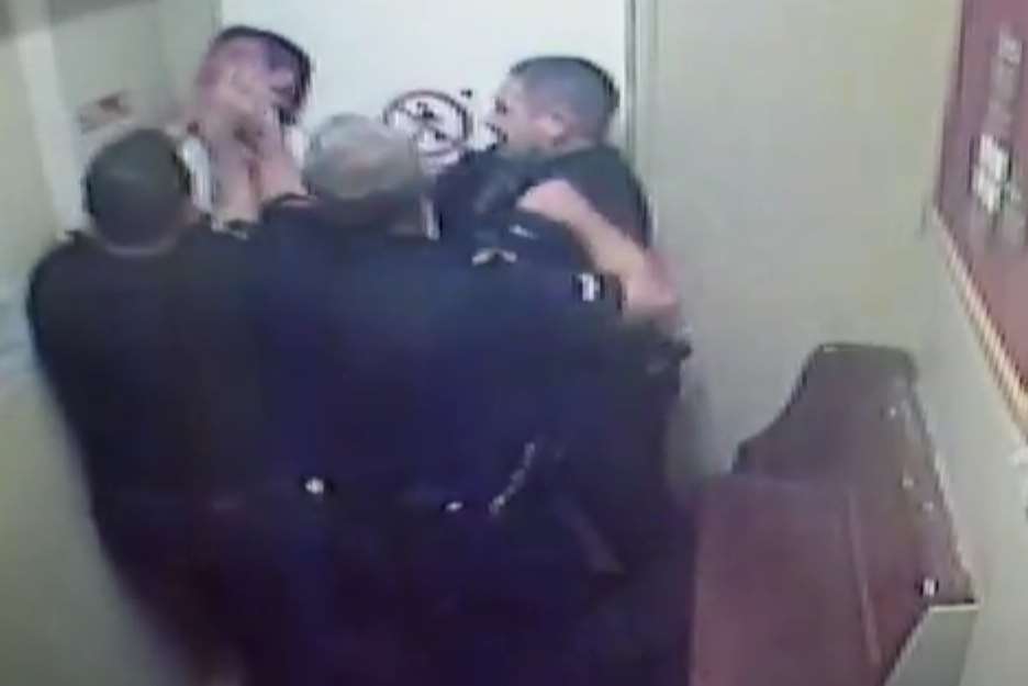 His head is forced upwards as one of the officers clenches his fist