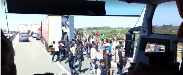 A swarm of about 40 men surround the lorry, which is stuck in Port bound traffic