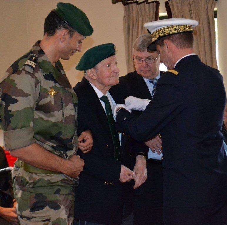 Francois Andriot stands to receive the honour, flanked by son John and Commander Amaury Desrivieres