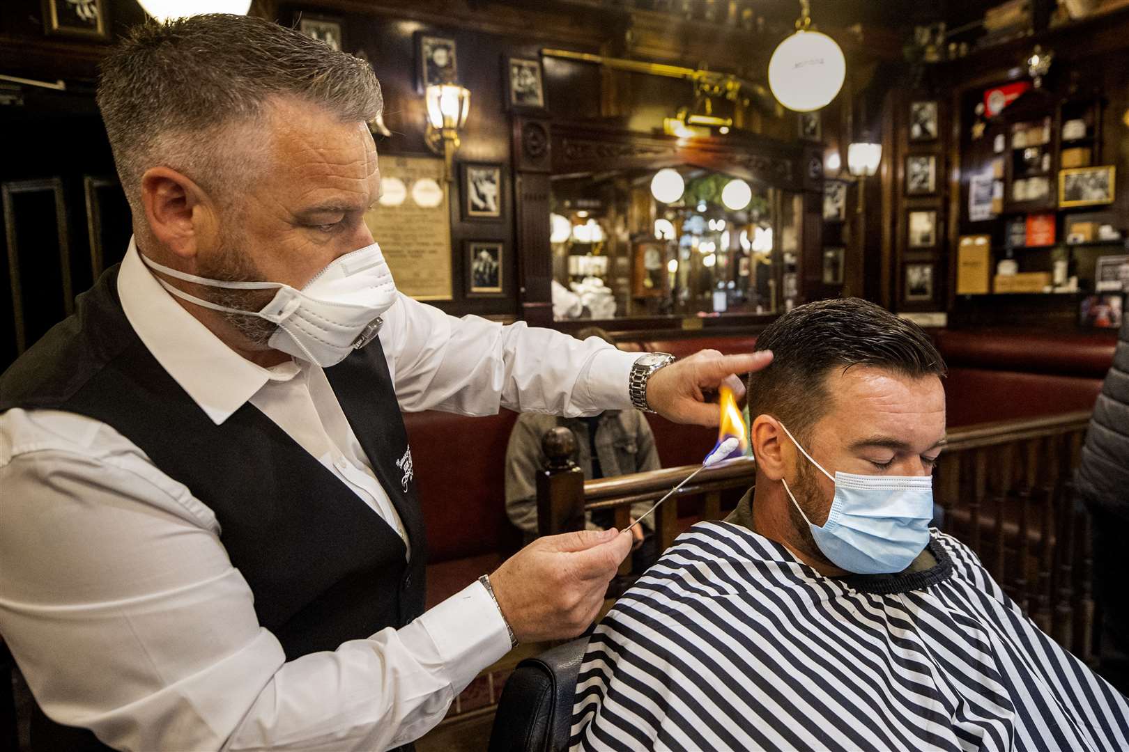 Sean Lawlor (left) singeing the hair of Damian Gilvary (right) during a haircut at Cambridge Barbershop on Belfast’s Lisburn Road. (Liam McBurney/PA)