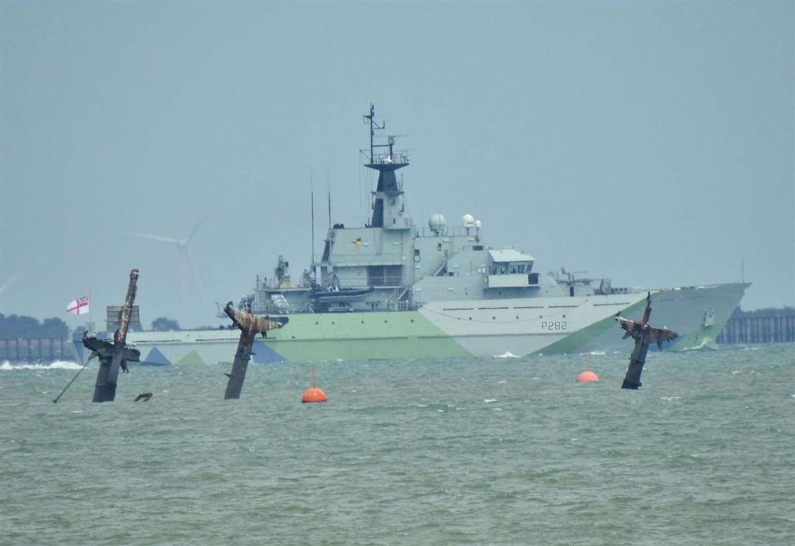 Camouflaged Royal Navy vessel passes wreck of bomb ship