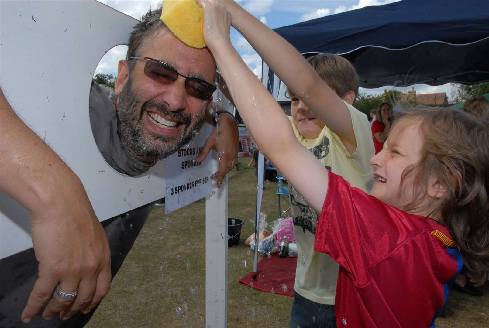 David Baddiel cools off in the stocks with a little help from Toby Woolston, 9, and Olivia Barletta, 8, at Rodmersham Primary School's fete. Picture: Mike Smith