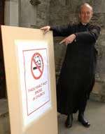 HOLY SMOKE: Fr Christopher Lindlar with the sign outside his church. Picture: DAVE DOWNEY