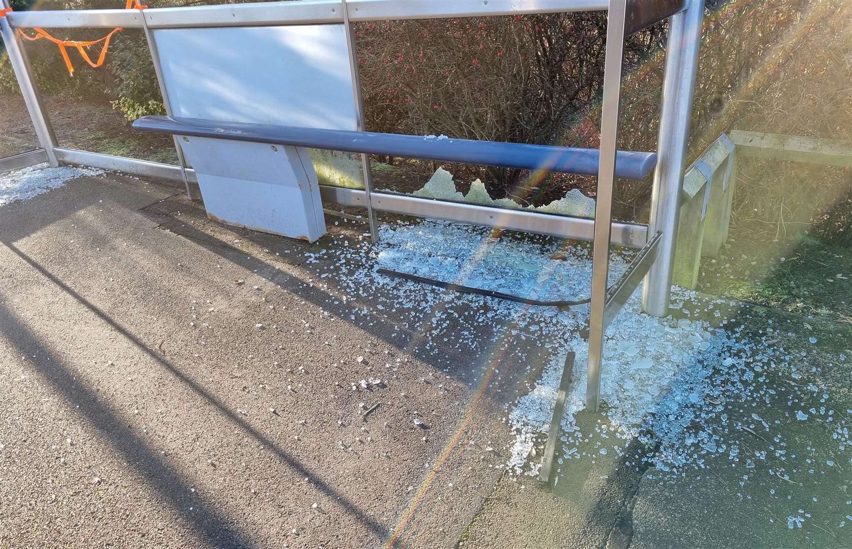 Shattered glass coats the pavement by the bus stop