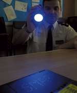Inspector Terry Chuter with an ultraviolet torch uncovers traces of SmartWater on a laptop computer