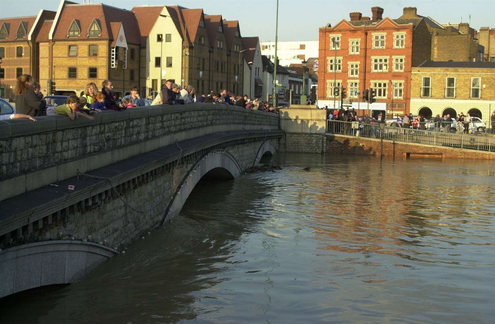 Crowds view the floods from Maidstone Bridge where the water is almost up with the top of the arches