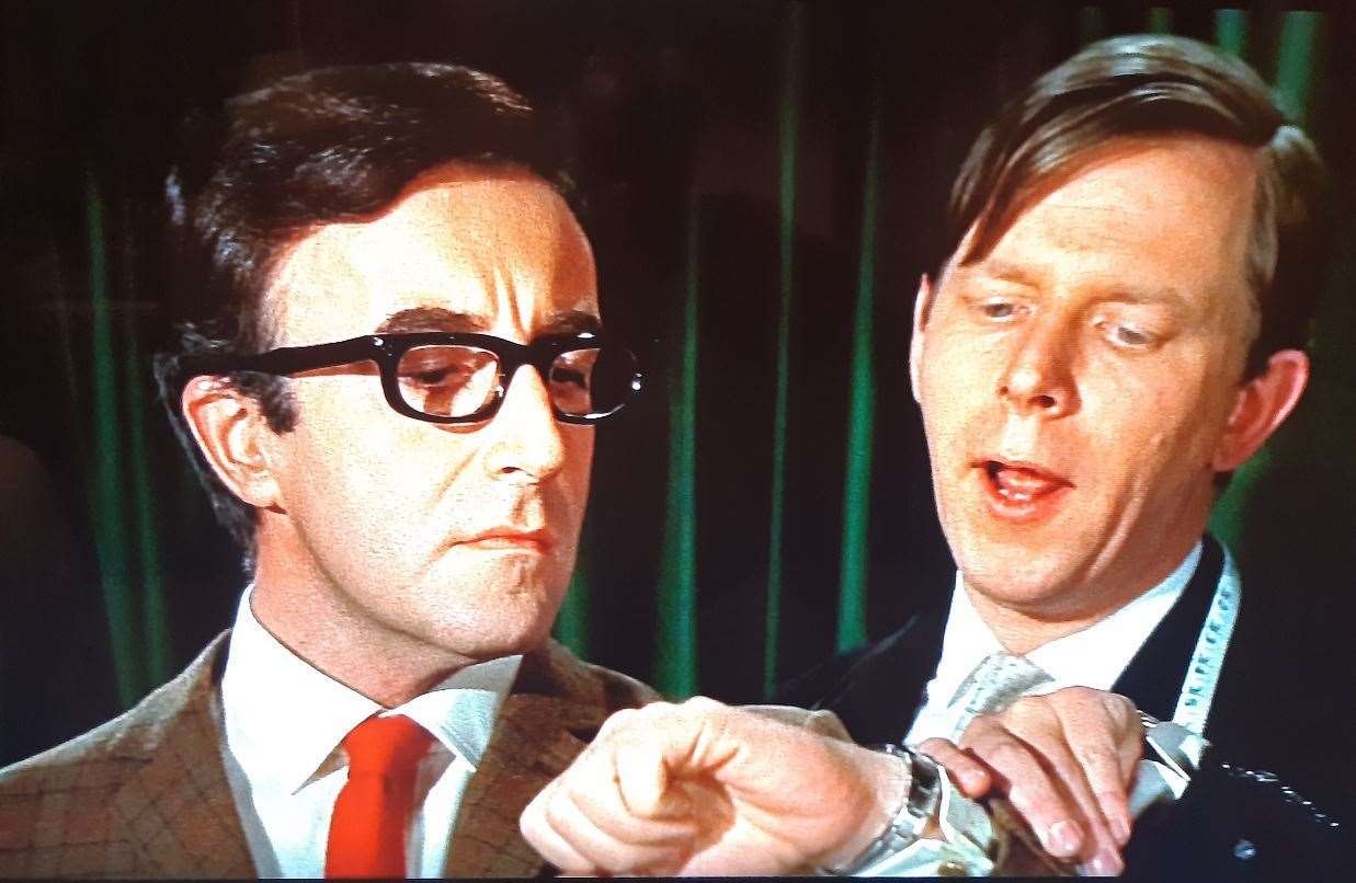 Peter Sellers, as James Bond, being fitted out with a tele-communicating watch by Q's assistant, John Wells