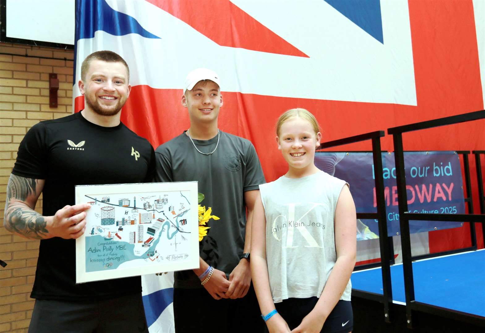 Young swimmers Florence and Albert present Adam Peaty MBE with a print created by local creative Designed by Esther. Picture: Medway Council