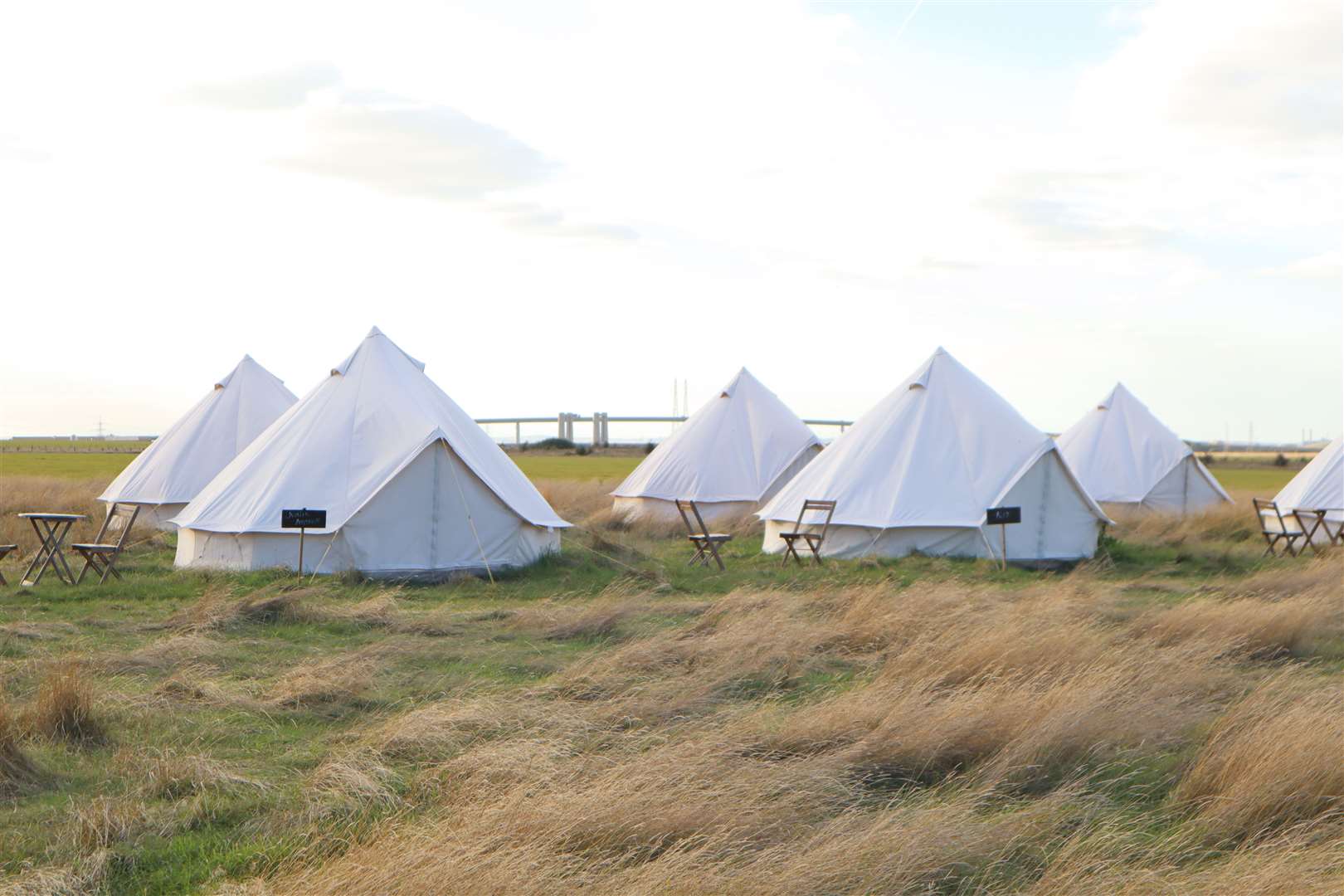 Glamping tents pitched in a field at Elmley Nature Reserve, Sheppey, with the Sheppey Crossing in the background