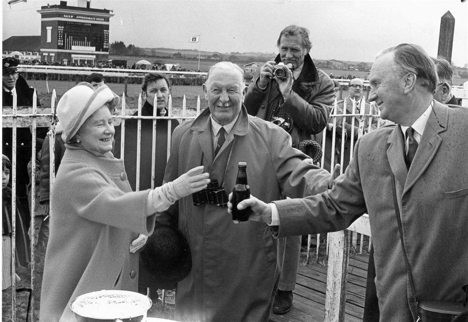 The Queen Mother enjoyed a joke with trainer Peter Cazalet at Folkestone Races in April 1970. When his horse, Cloudsmere, won the Whitbread 'Elephant' handicap Chase she handed him a bottle of County Ale as a token of the crates of beer due to the winning stable. Also in the picture is Lord Cornwallis, Lord Lieutenant of Kent