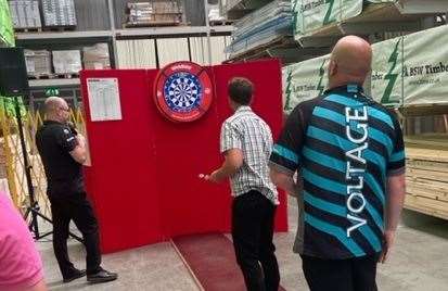 Former world champion darts player Rob Cross looks on as the KM's Luke Cawdell toes the oche