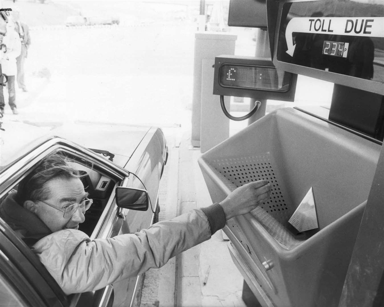 Way before the dart charge online payments were introduced, a driver drops some coins in a toll booth at the Dartford Tunnel in August 1985