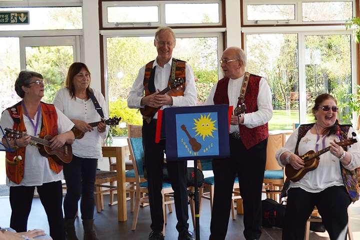 The Sunshine Ukes playing at Pilgrims Hospice therapy centre in Canterbury when they presented a cheque.