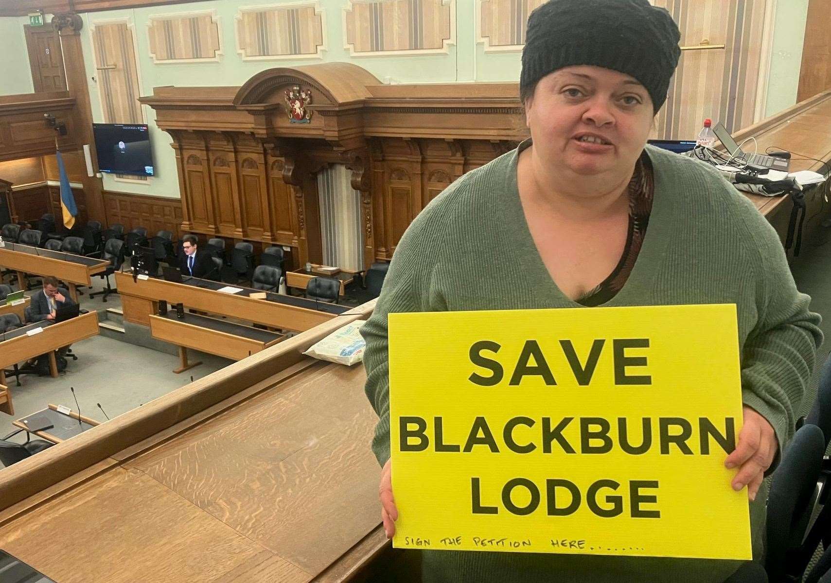 Cllr Dolley Wooster in the chamber at County Hall with her placard demanding Blackburn Lodge is retained