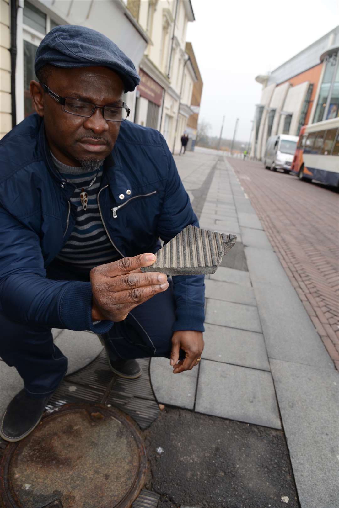 Gary George the owner of Papa G barbers examines a piece of the cracked Flume paving outside shop