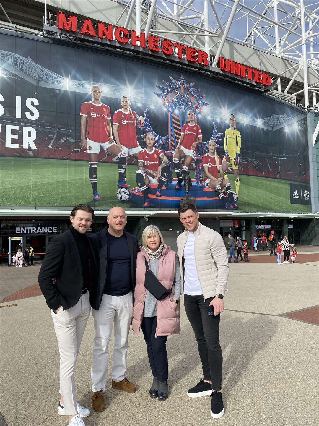 Brothers Luca and Giorgio flank dad Mario and mum Carol in front of a giant poster of Alessia Russo and her Manchester United team-mates outside Old Trafford