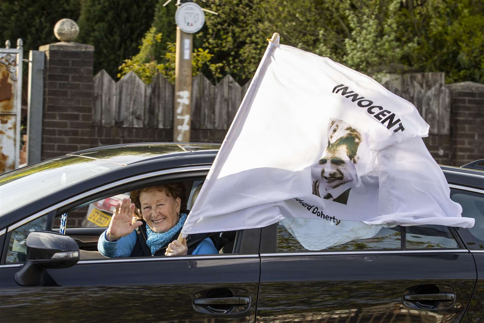 One of the cavalcade of cars passing through Ballymurphy, with a white flag bearing victim Edward Doherty’s picture and the word innocent (Liam McBurney/PA)