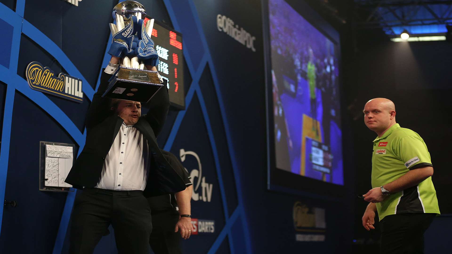 Lee Marshall holds the Sid Waddell trophy aloft in front of the eventual winner Michael van Gerwen. Credit: Steve Paston/PA Wire.