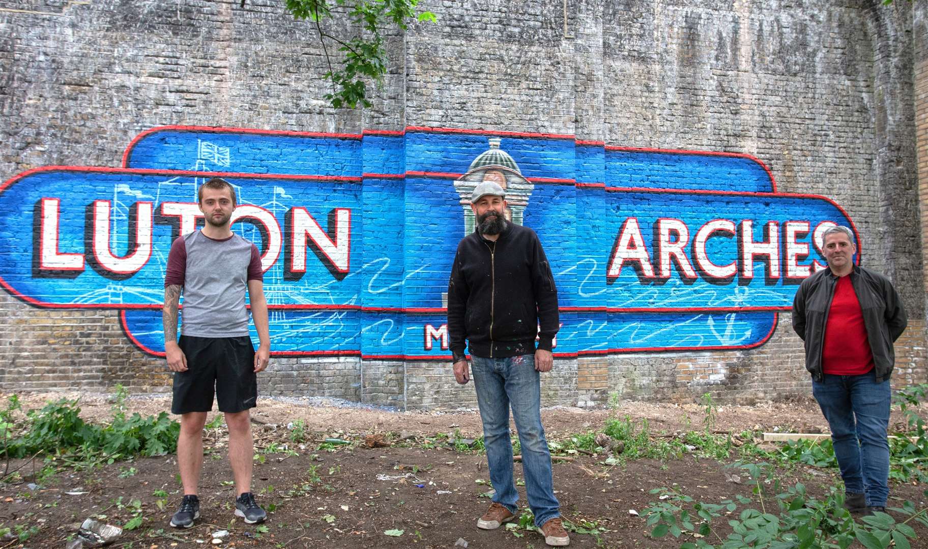 Artist Lionel Stanhope (centre) with a mural he created in the area, with Jackson Fraser-Hague and Stephen Perez from Arches Local