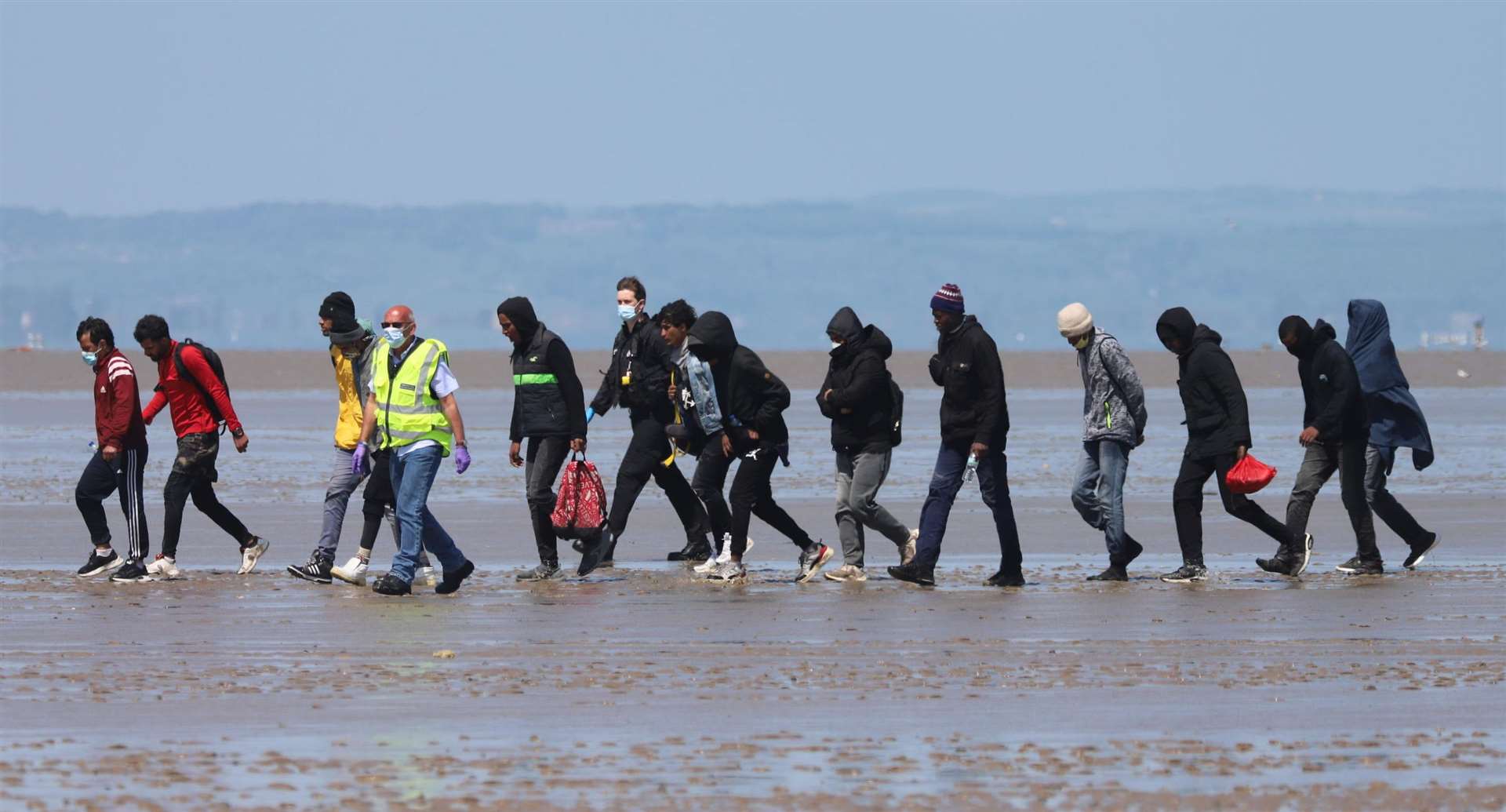 Asylum seekers are led ashore by officials at Romney Marsh