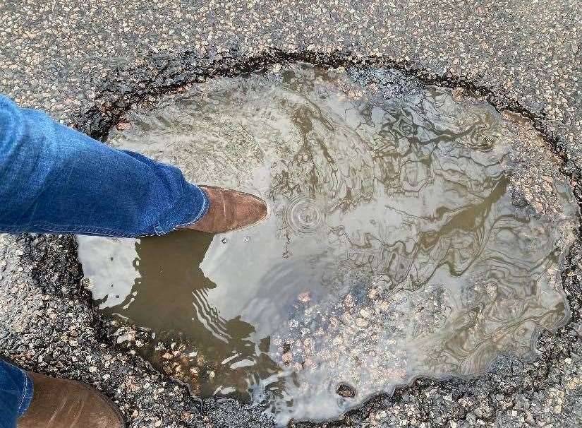 Someone demonstrates the depth of the pothole
