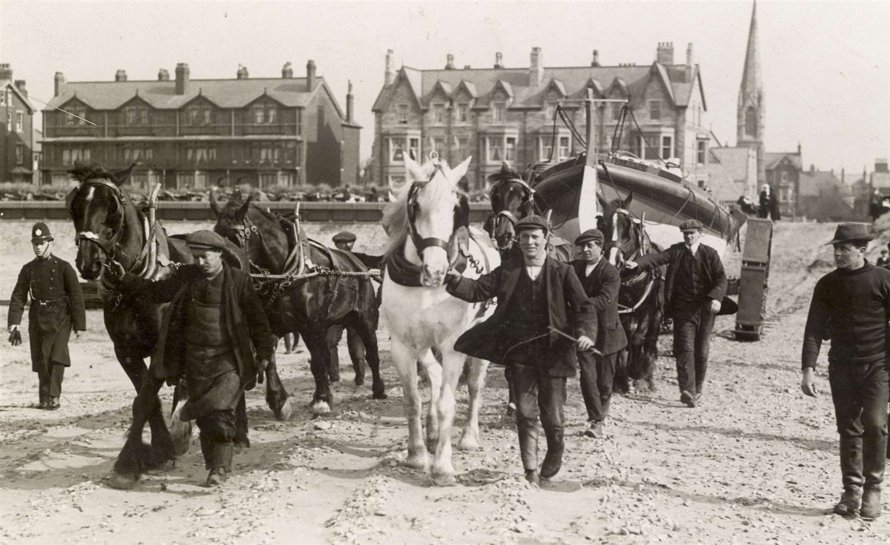 A horsedrawn launching trailer pulls a lifeboat towards the sea escorted by policeman. Image: RNLI.