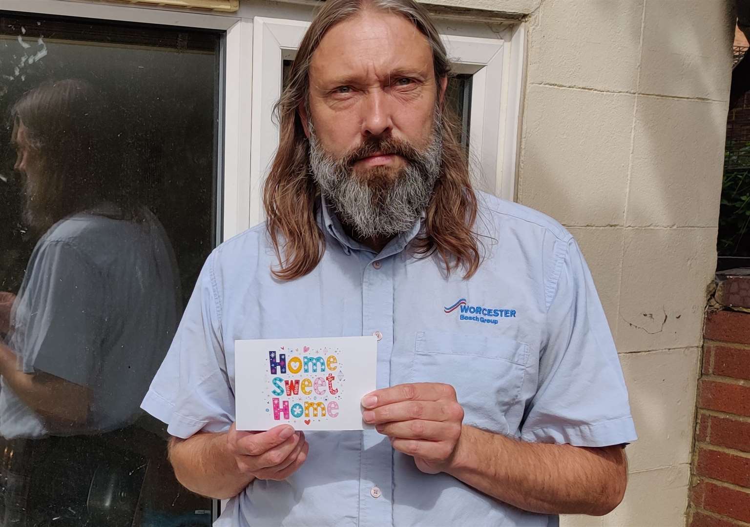 Nik Ross stood outside his flooded-out home with the 'Home Sweet Home' card