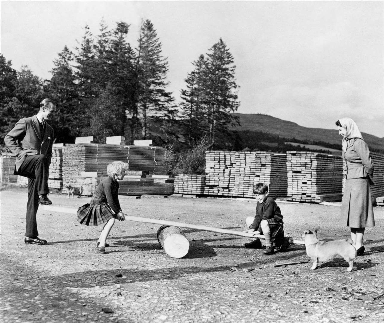 Prince Charles and Princess Anne, watched by the Queen and the Duke of Edinburgh, play on a see-saw made from a log and a plank of wood on the Balmoral Estate in 1957 (PA)