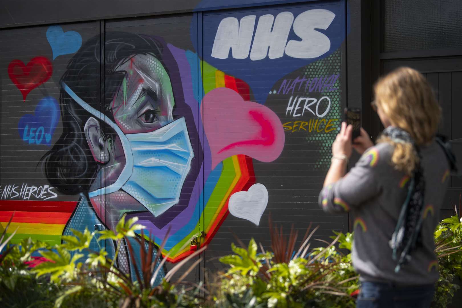 A woman takes a photograph of graffiti in support of the NHS in south-east London (Victoria Jones/PA)