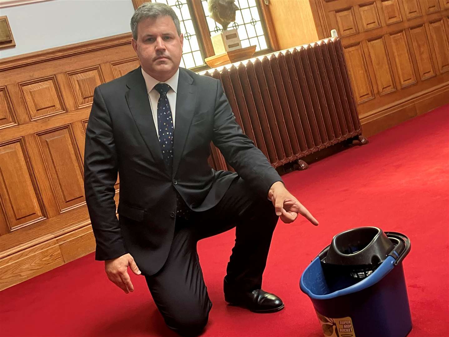 Lib Dem leader Cllr Antony Hook pointing to a bucket collecting water from the leaking roof at County Hall in Maidstone