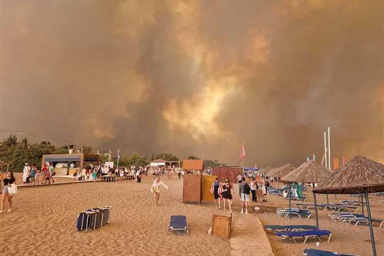 Tourists take refuge on the beach as smoke arises over a resort on Rhodes. Picture Leigh Buckwell