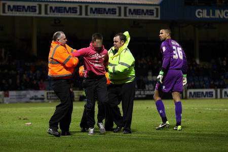 The Gills fan is detained by stewards while Wycombe keeper Jordan Archer looks on.