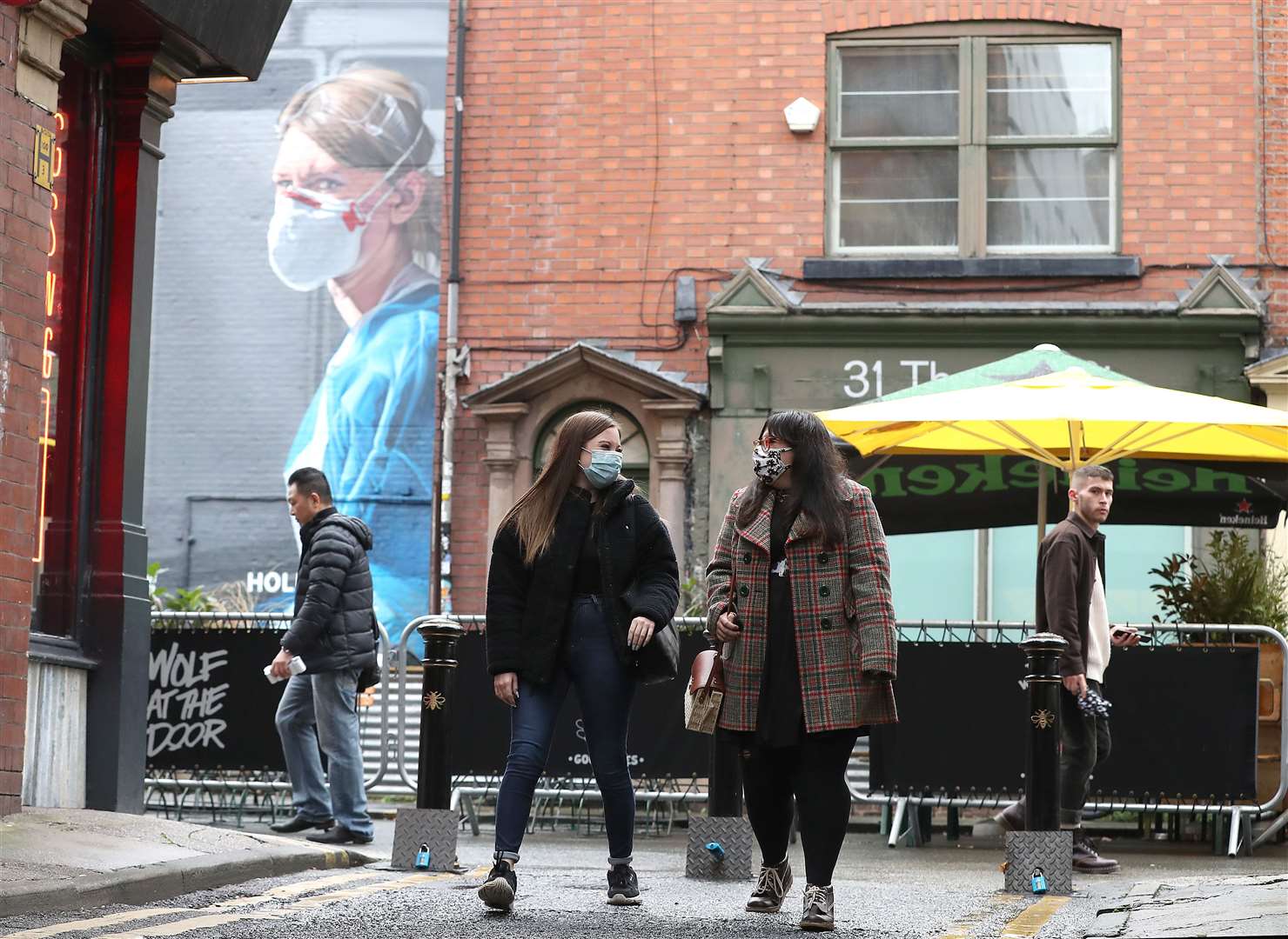 People wearing a face mask walk near a mural of a nurse in the Northern Quarter of Manchester (Martin Rickett/PA)